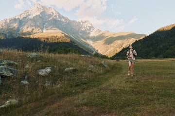 Naklejka premium Woman hiker stands in a grassy valley with rugged mountains in the background, wearing hiking gear. A lifestyle moment of outdoor exploration and adventure.