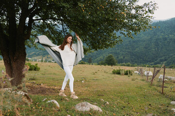 Naklejka premium Young woman in white outfit posing outdoors under a leafy tree in a rural field. Lifestyle photography showing freedom, nature, and calm, with soft daylight and relaxed movement.