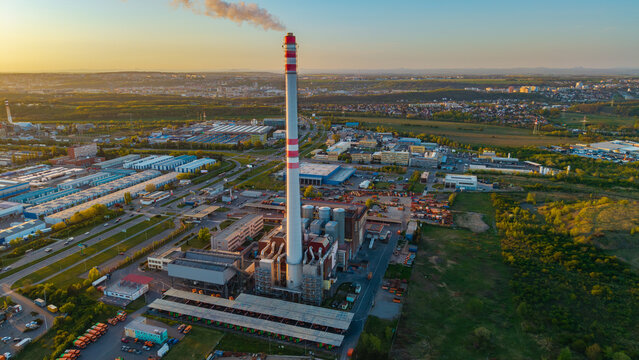 Aerial view of the Malesice Infrastructure Objects featuring a tall industrial chimney with red stripes and smoke during sunset in Prague, Hlavni mesto Praha, Czechia.