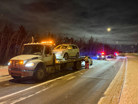 Tow truck loading a disabled vehicle on a snowy roadway at night with police vehicles responding in Alberta, Canada.