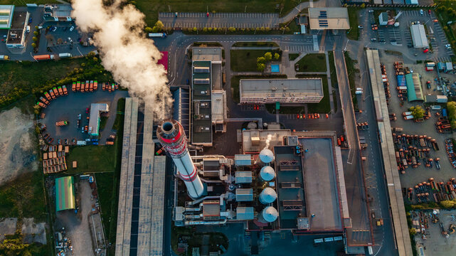 Aerial view of Malesice Infrastructure Objects featuring a tall chimney emitting smoke and rows of orange trucks in Prague, Hlavni mesto Praha, Czechia.