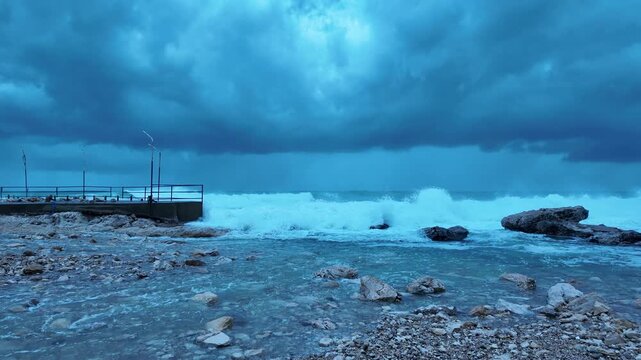 Giant Wave Wall Rushing Toward Coast &ndash; Powerful Storm Surge Flooding Rocky Beach Near Coastal Pier