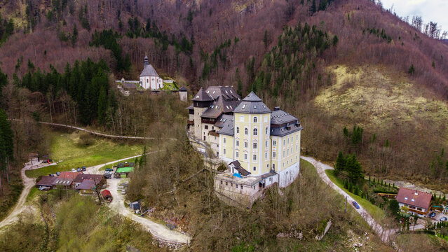 Aerial view of Klaus Castle and a hillside chapel surrounded by dense mountain forest in Klaus an der Pyhrnbahn, Upper Austria, Austria.