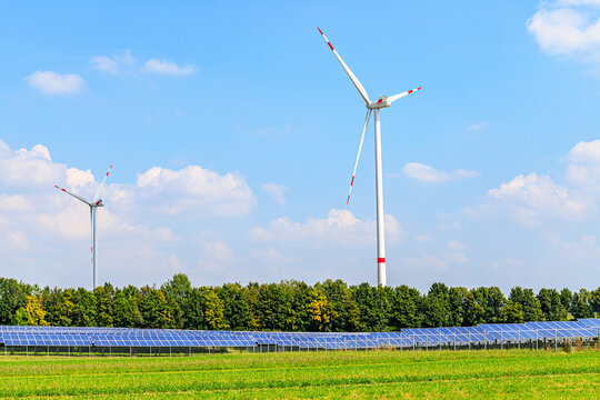 Wind turbines and solar panels contribute to renewable energy production in a green field in summer