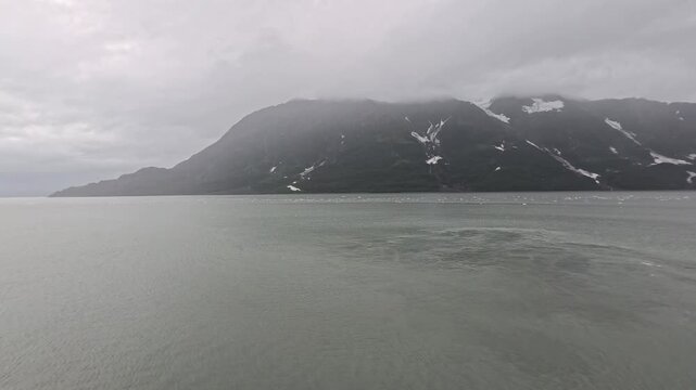 Alaska, USA - Hubbard Glacier meets Disenchantment Bay, forming a dramatic landscape where ice calves into the water below cloudy mountains. Misty conditions enhance the region. 