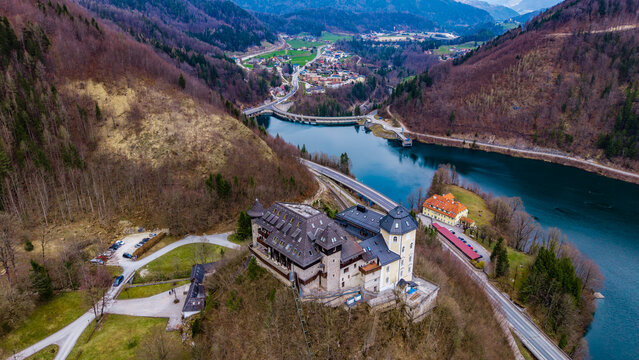 Aerial view of Klaus Castle overlooking the turquoise waters of the Klauser Stausee reservoir and the surrounding forested mountains in Klaus an der Pyhrnbahn, Upper Austria, Austria.