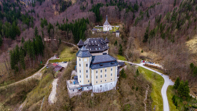 Aerial view of Klaus Castle with its historic architecture and dark roofs, surrounded by dense forests and a small chapel in Klaus an der Pyhrnbahn, Upper Austria, Austria.