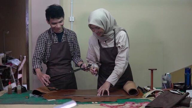 Asian partners inspecting leather product prototype, female hijab designer and male colleague examining pattern and sample,