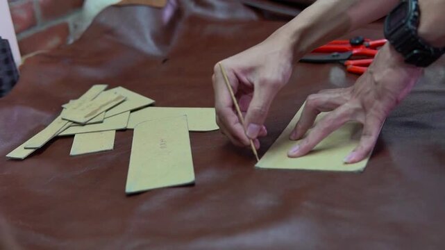 Hands marking cardboard patterns on leather workbench with precision awl and scissors closeup of fingers, watch, stacked