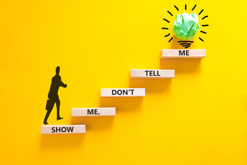 Tell or show symbol. Concept words Show me, do not tell me on beautiful wooden blocks. Beautiful yellow paper background. Light bulb icon. Businessman icon. Business tell or show concept. Copy space. © Dzmitry