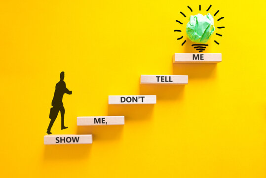 Tell or show symbol. Concept words Show me, do not tell me on beautiful wooden blocks. Beautiful yellow paper background. Light bulb icon. Businessman icon. Business tell or show concept. Copy space.