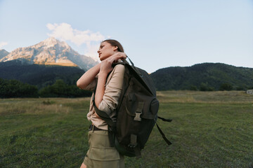 Fototapeta premium A young woman with a backpack walks across a meadow toward distant mountains, feeling free, focused, curious, and ready for adventure.