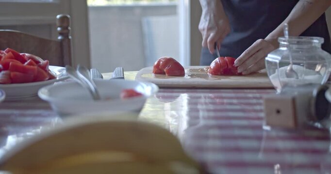 Skilled hands meticulously slice ripe, red tomatoes on a rustic wooden cutting board. This close-up footage highlights the freshness and precision of home cooking.