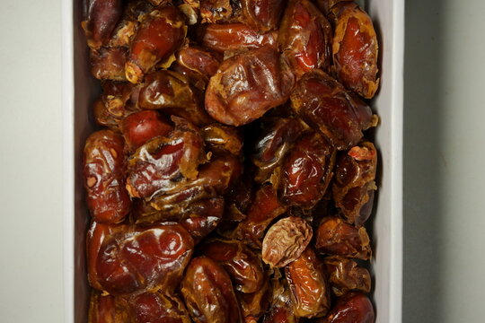 High angle shot of sweet dried dates packed in a white box. The dates have a glossy texture and rich brown color, perfect for healthy snack or Ramadan food concepts.