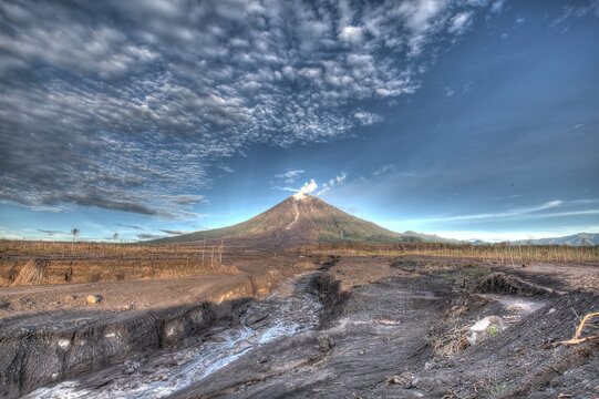 Dreadful landscape of Mount Semeru's volcanic mudflow path in East Java, Indonesia. The image captures the aftermath of an eruption with cold lava deposits and destroyed land under a dramatic sky
