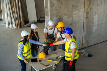 Fototapeta premium Unified construction team putting hands together in a huddle over a table on site.