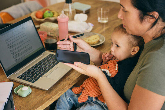 Woman multi-tasking by taking care of daughter and doing office work on laptop at home