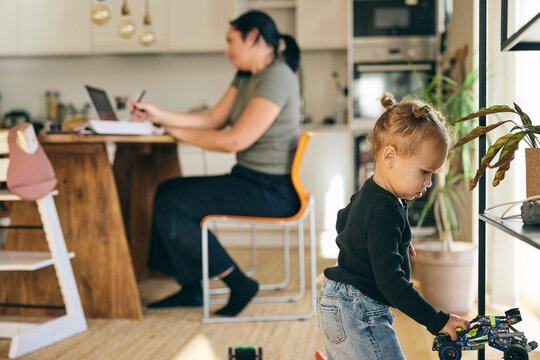 Cute girl playing with toy while mother working from home on laptop