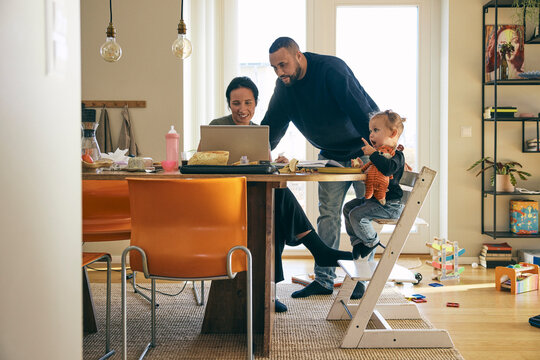 Girl having breakfast while sitting beside parents using laptop at home