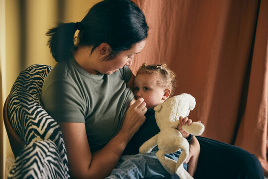 Mother breastfeeding daughter while sitting on armchair at home