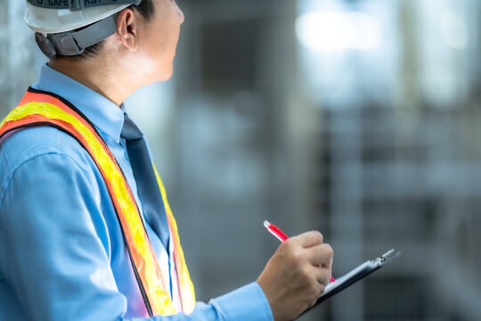 A focused quality control inspector in safety gear and hard hat meticulously recording data on a clipboard in an industrial plant environment.