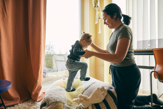 Mother holding hand of daughter jumping on bean bag in home