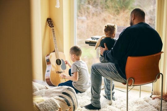 Father spending leisure time with kids playing with musical instruments at home