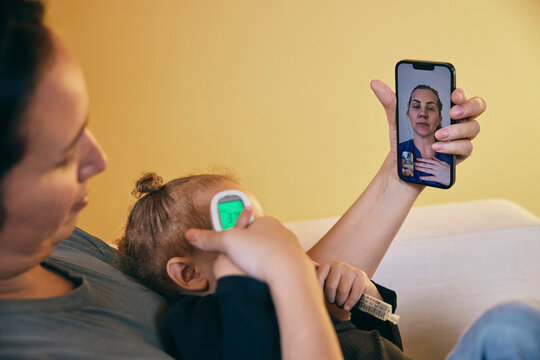 Female pediatrician on video call advising mother checking body temperature of daughter having fever at home