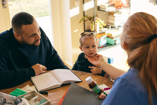 Female doctor examining girl sitting with father during home visit