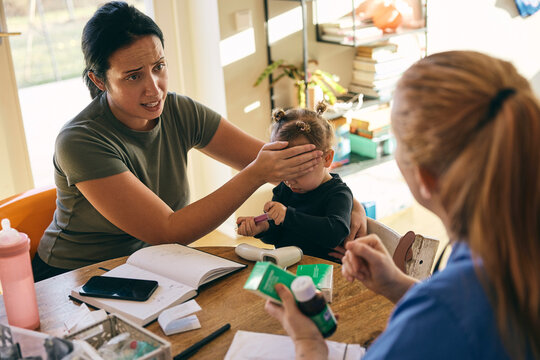 Mother explaining daughter's body temperature due to high fever to female nurse visiting at home
