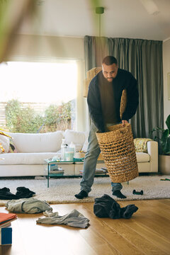 Man collecting dirty clothes from floor in laundry basket while doing chores at home