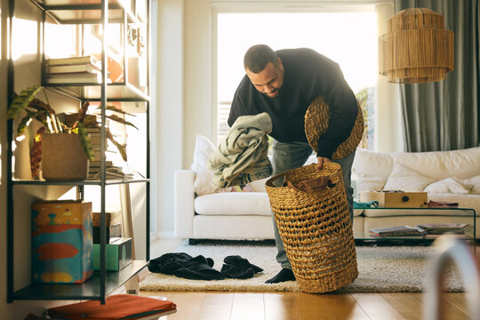 Man collecting dirty clothes in laundry basket while doing chores at home