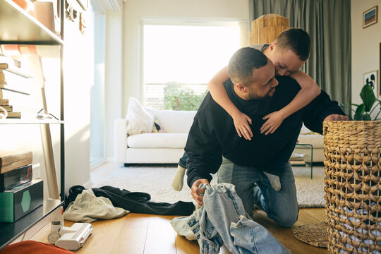 Father piggybacking son while collecting dirty clothes in laundry basket at home
