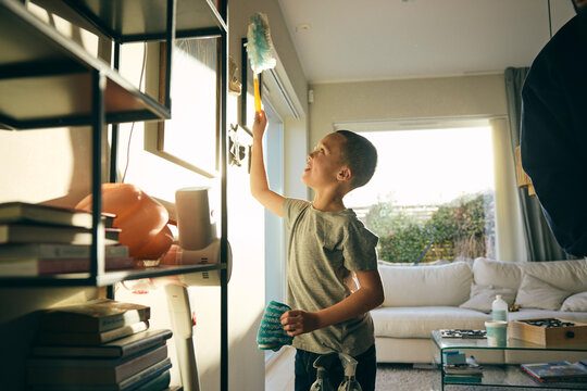 Elementary boy helping father in cleaning picture frame while doing house chores