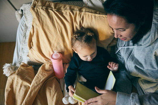 Directly above shot of mother showing picture book to daughter while lying on bed in home