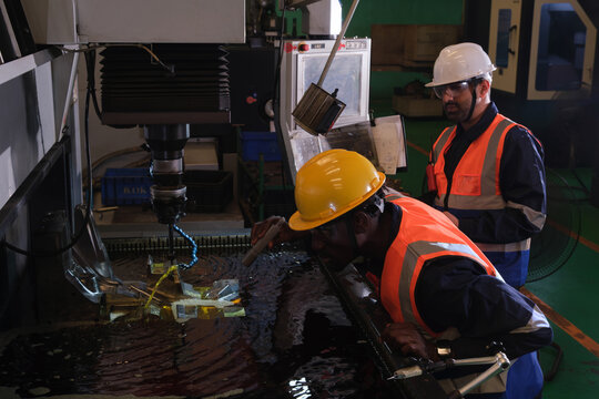 Workers perform machining tasks in a workshop using CNC machine and monitoring water coolant in the evening hours