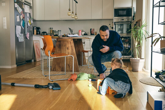 Full length of father taking through wireless in-ear headphones while playing with daughter at home