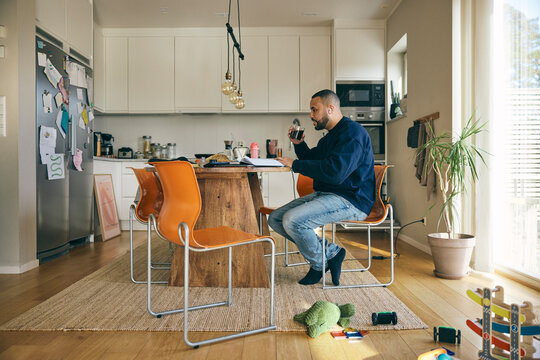 Male freelancer drinking coffee while working on laptop from home