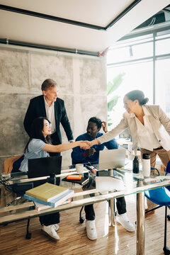 Investors doing handshake with employees sitting at desk in modern office