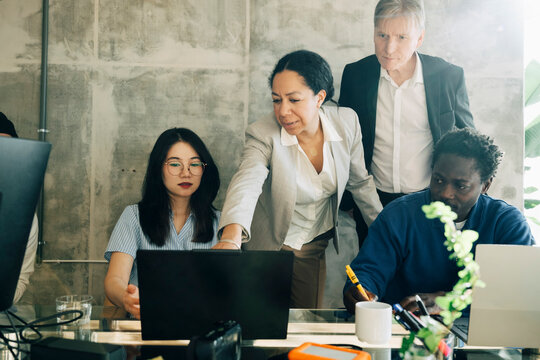 Businesswoman pointing at laptop during discussion with employees at office