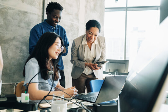 Group of business professionals smiling while looking at laptop screen in modern office