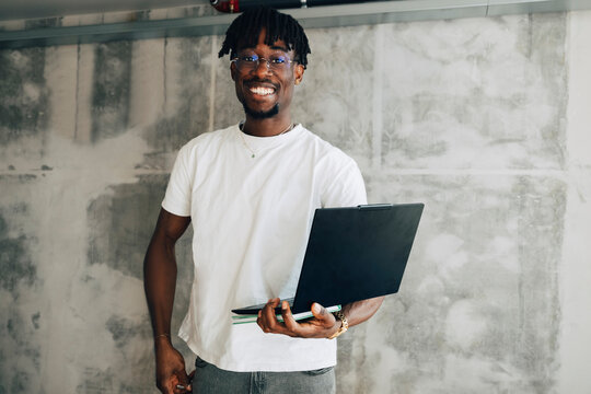 Portrait of confident businessman holding laptop while standing against wall in office