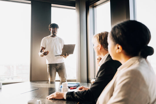 Businessman holding laptop and talking to his team during meeting at office