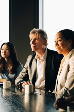Group of male and female investors sitting at table during team meeting at modern startup office