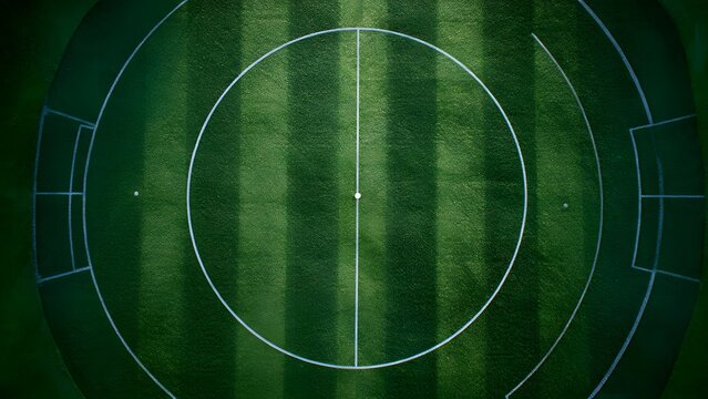 Top down aerial view of circular green australian rules football field with center circle and markings from high altitude drone shot with bright stadium lighting
