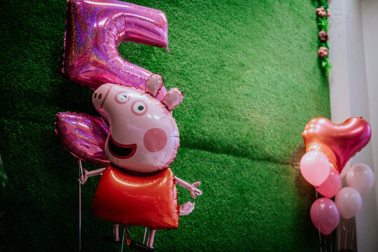Peppa Pig balloon with number five and heart-shaped balloons against a green grass backdrop for a birthday celebration