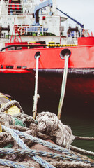 Fototapeta premium weathered mooring ropes and knots on a pier, with a large red industrial ship docked in the background