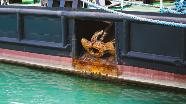 Horizontal close up of a ship  dark hull with a rusty anchor in the hawsehole