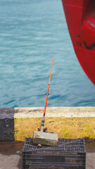 Fototapeta premium An orange fishing rod held by a stone on a pier next to a large red ship