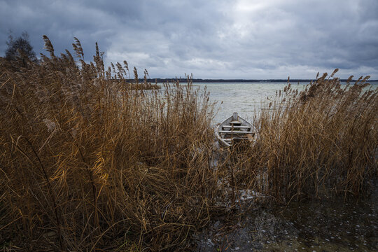 Old rural wooden, fishing boat is moored on the shore of a lake. A gloomy windy day